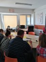 Zdjęcie 4 zajęć warsztatowych z zakresu coachingu zawodowego. Na zdjęciu widoczna osoba prowadząca oraz uczestnicy spotkania, którzy siedzą przy okrągłym stole.