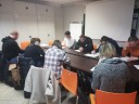 Zdjęcie 1: Grupa osób siedząca i pisząca przy stole podczas zajęć grupowych pod nazwą „KOMPENDIUM  RYNKU PRACY"