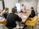 Zdjęcie 2: grupa osób siedząca przy stole podczas warsztatów pod tytułem: „Ucz się, zarządzaj, zarabiaj – wiedza Twoim atutem"