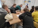 Zdjęcie 2: grupa osób siedząca przy stole podczas grupowej informacji zawodowej pod nazwą „Kompendium rynku pracy.”